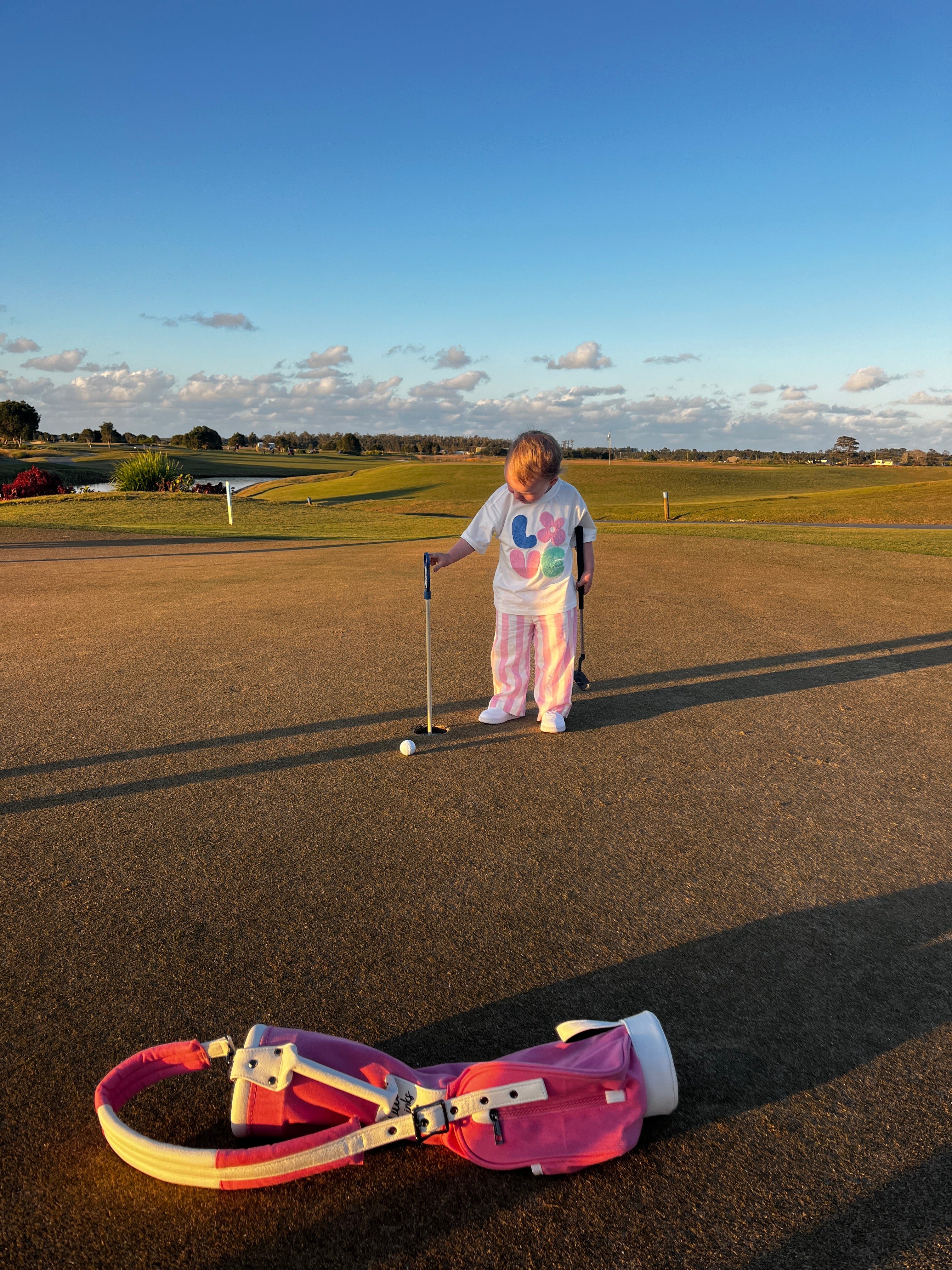 Toddler putting at the golf course with her pink toddler golf bag in the foreground